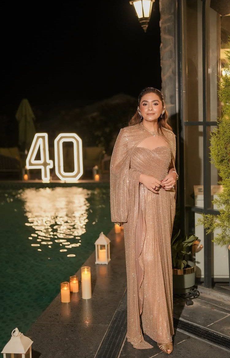 Woman in a shimmering gold gown posing by a pool with glowing 40 numbers