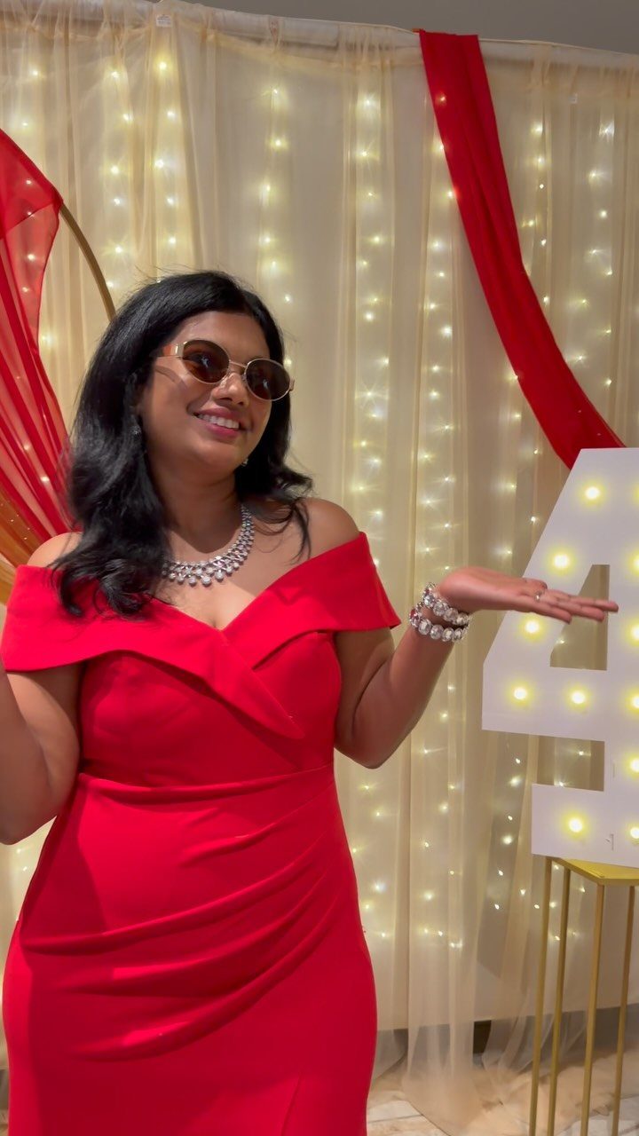 Plus-size woman in a red off-the-shoulder dress posing by a birthday backdrop