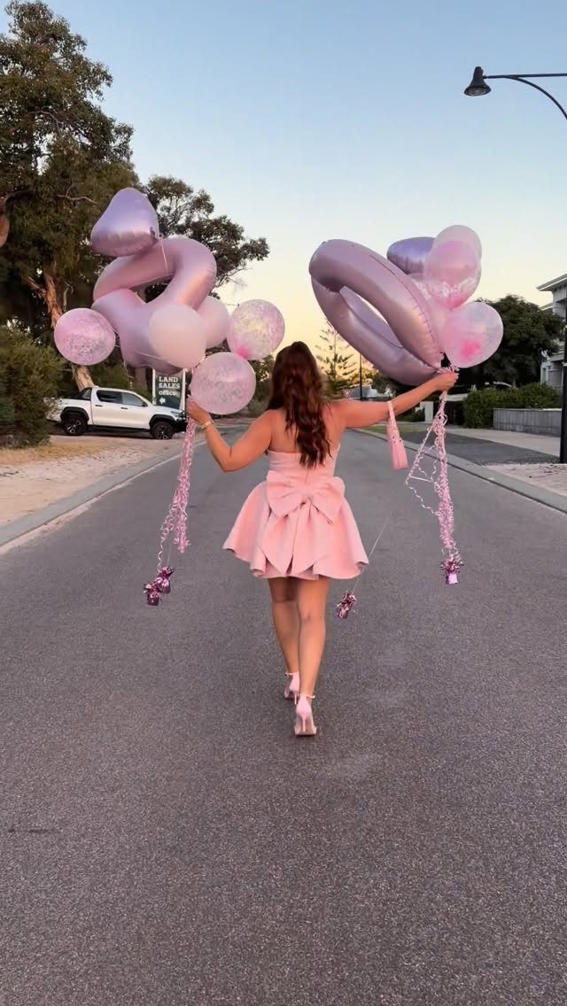 Plus-size woman in a pink dress holding purple number 40 balloons on a street