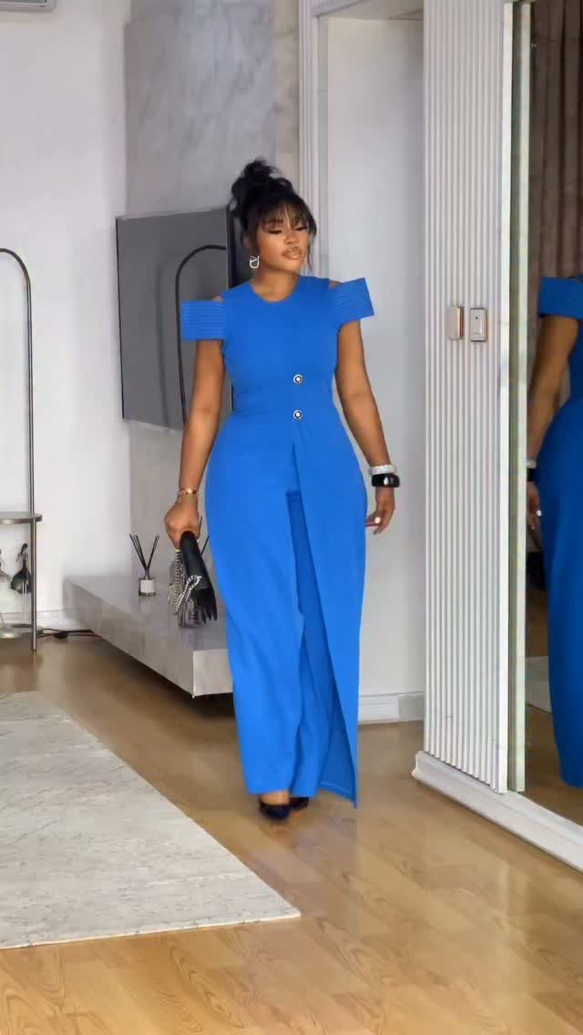 Plus-size woman in a royal blue tailored jumpsuit with off-the-shoulder sleeves and wide legs.