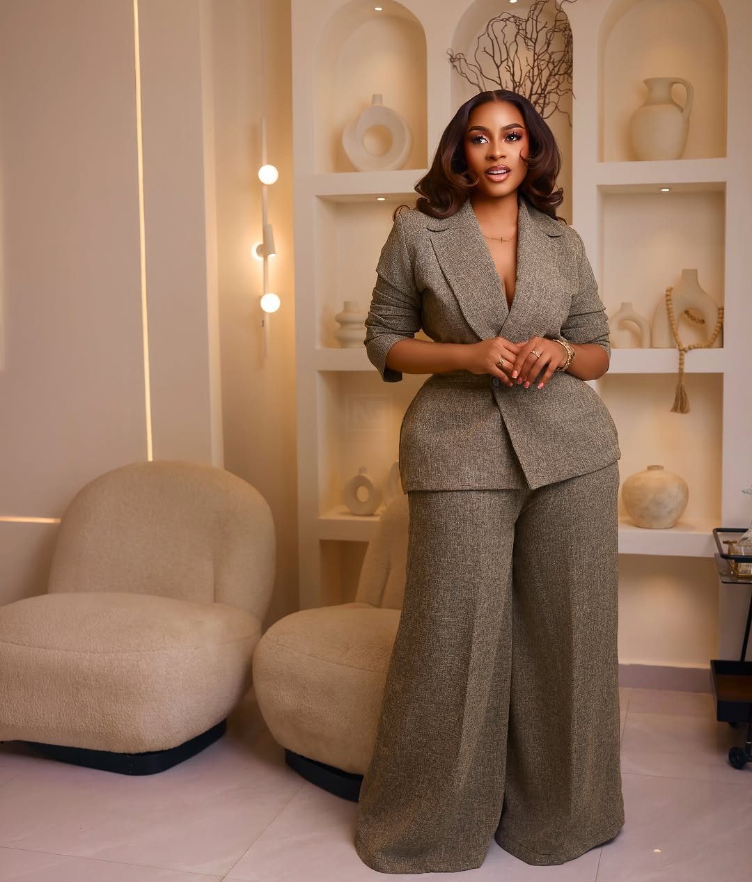 Plus-size woman wearing a tailored olive-brown blazer and wide-leg trousers in a modern room.