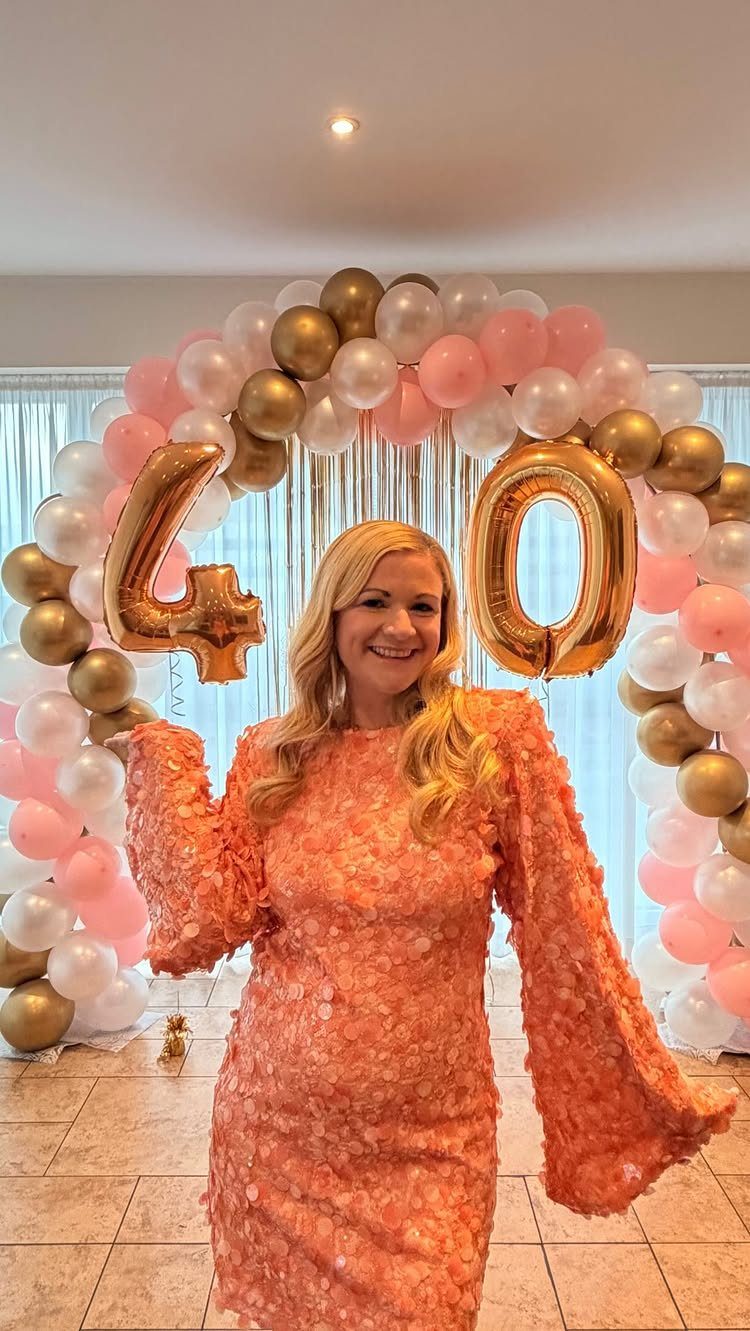 Plus-size woman in a peach textured dress posing before 40th birthday balloons.