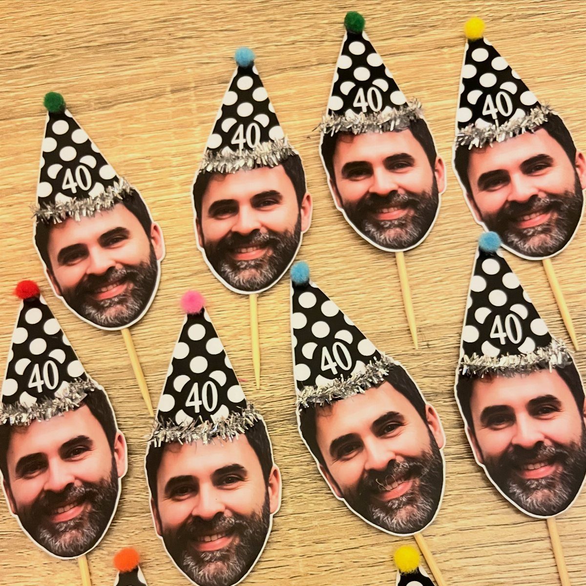 Cutout faces of a man wearing 40th birthday hats on wooden sticks.