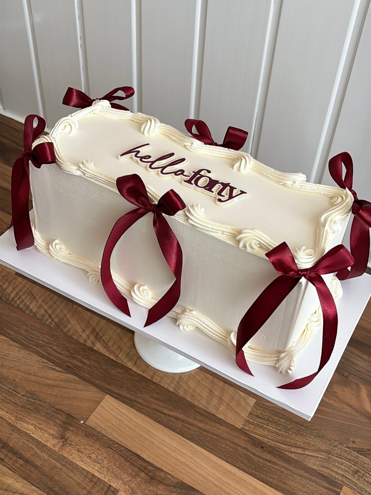 White rectangular sheet cake with red bows and hello forty written in red.
