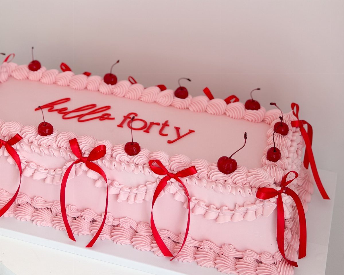 Pink frosted sheet cake with red ribbons, cherries, and 'hello forty' text.