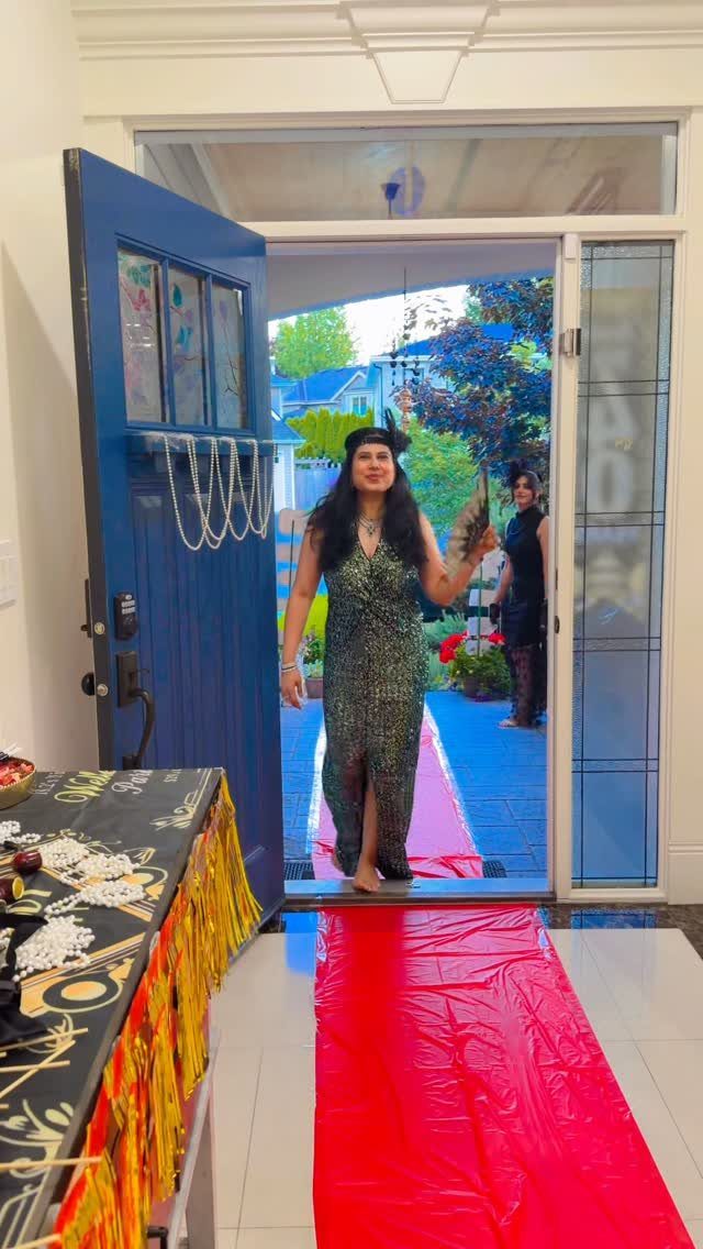 Woman in a green flapper dress standing on a red carpet in a doorway.