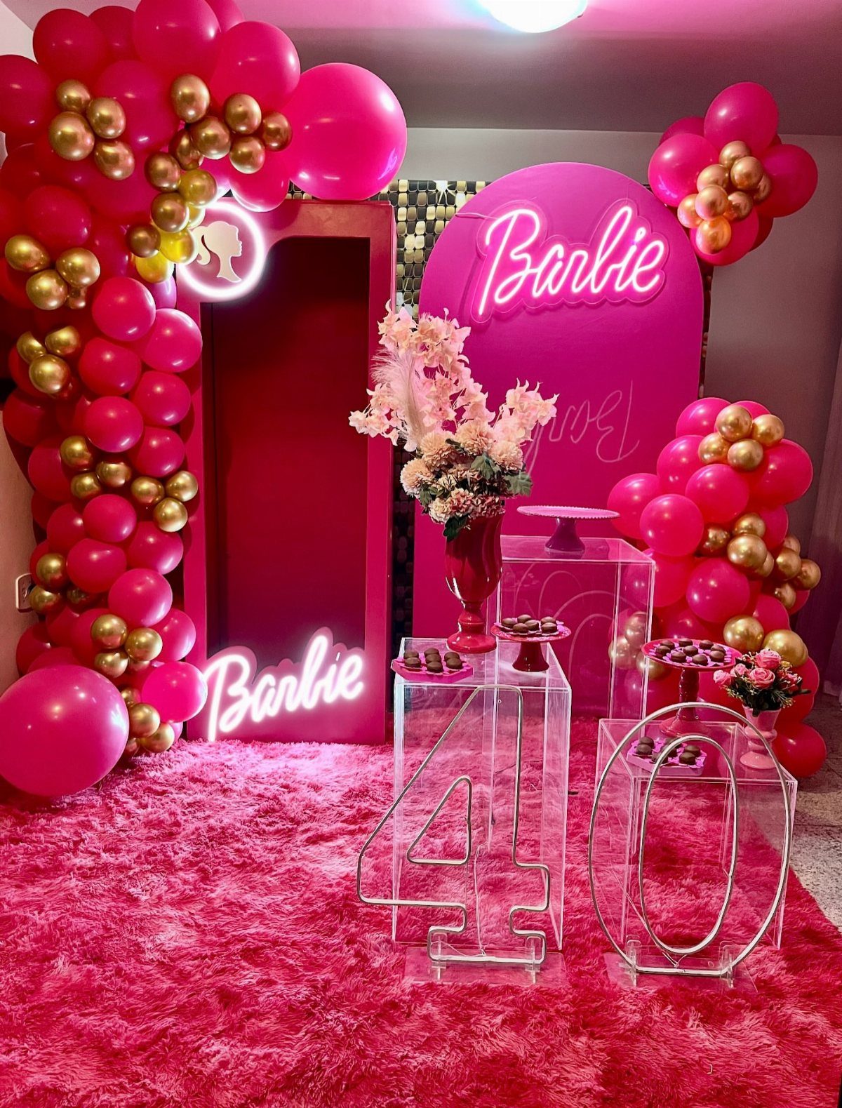 Pink Barbie-themed 40th birthday party setup with balloons, neon signs, and illuminated numbers.