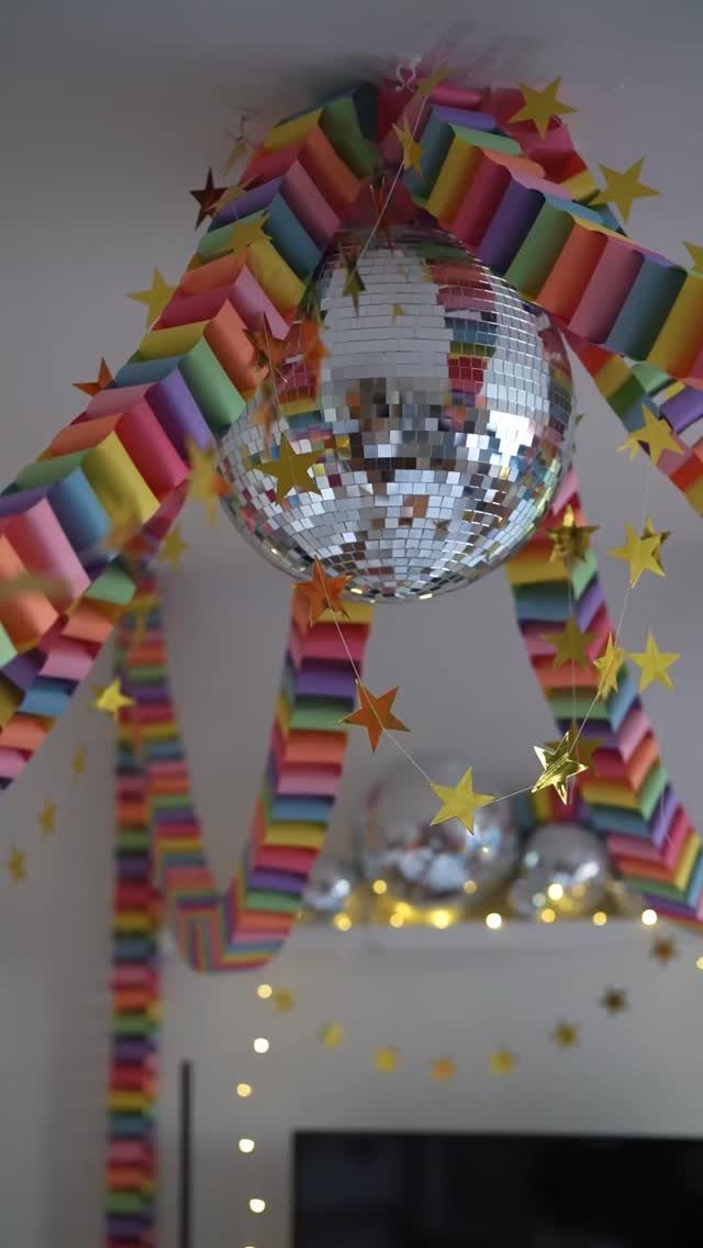 Mirrored disco ball surrounded by rainbow streamers and gold stars for a party.