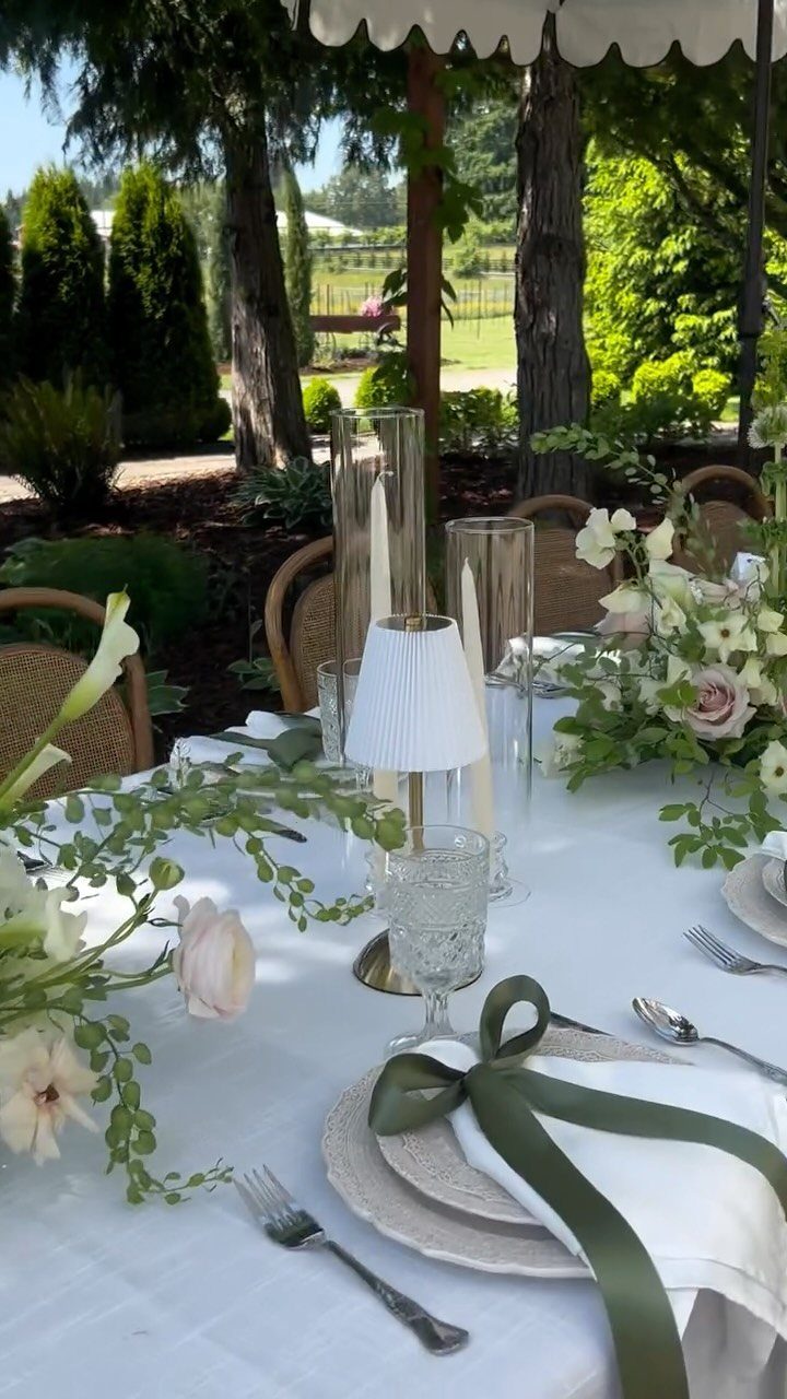 Elegant outdoor table setting with white flowers and green ribbons in a garden.