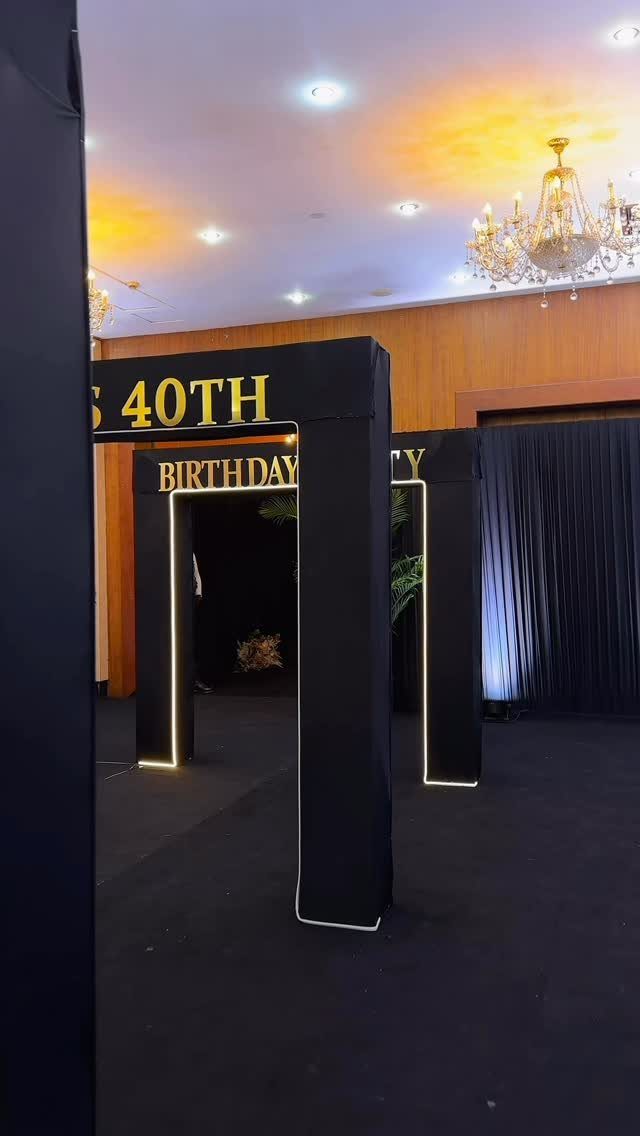 Black 40th birthday party entrance arch with gold lettering and white LED lighting.