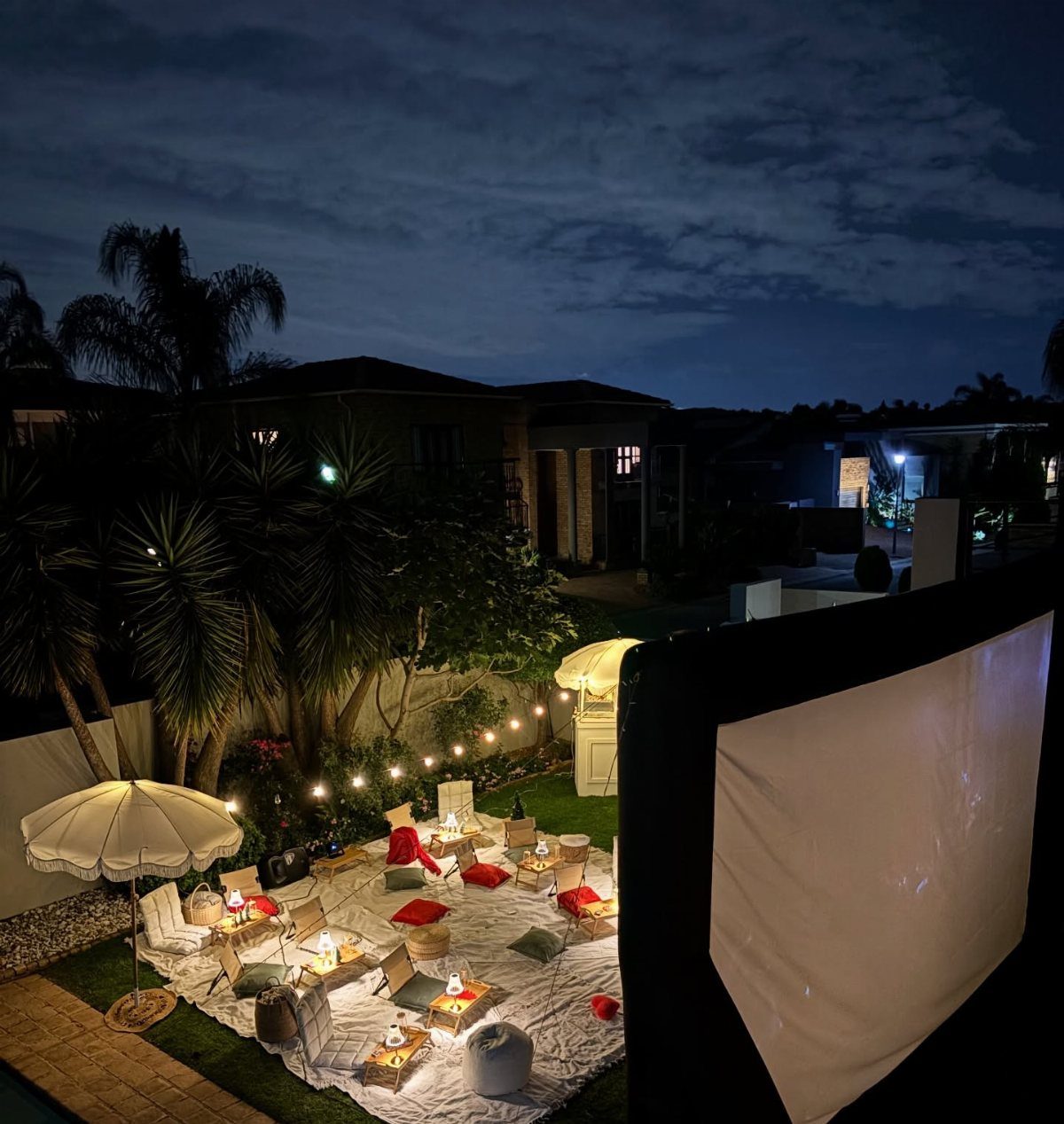 Outdoor movie setup with a large projector screen, white blanket, and cozy cushions.