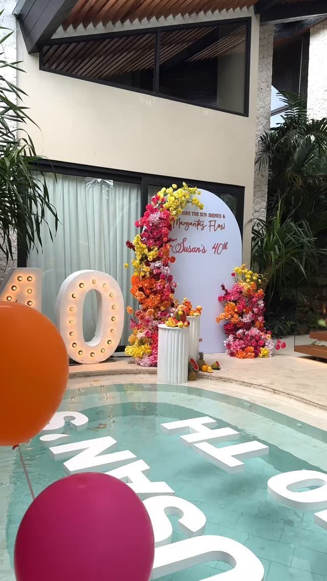 Outdoor 40th birthday celebration with illuminated numbers, floral backdrop, and pool decorations.