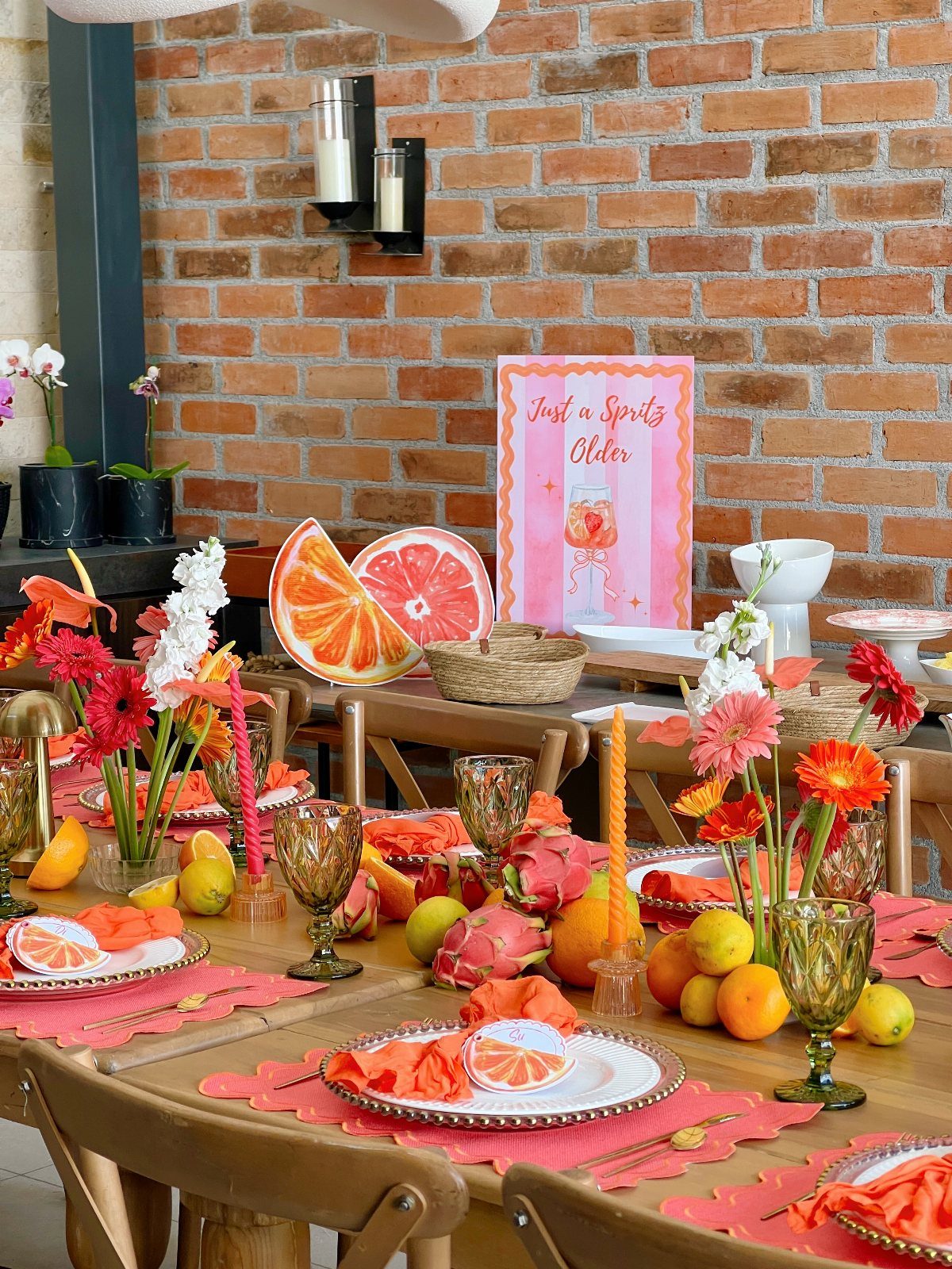 Festive brunch table with citrus fruits, orange flowers, and a celebratory sign.