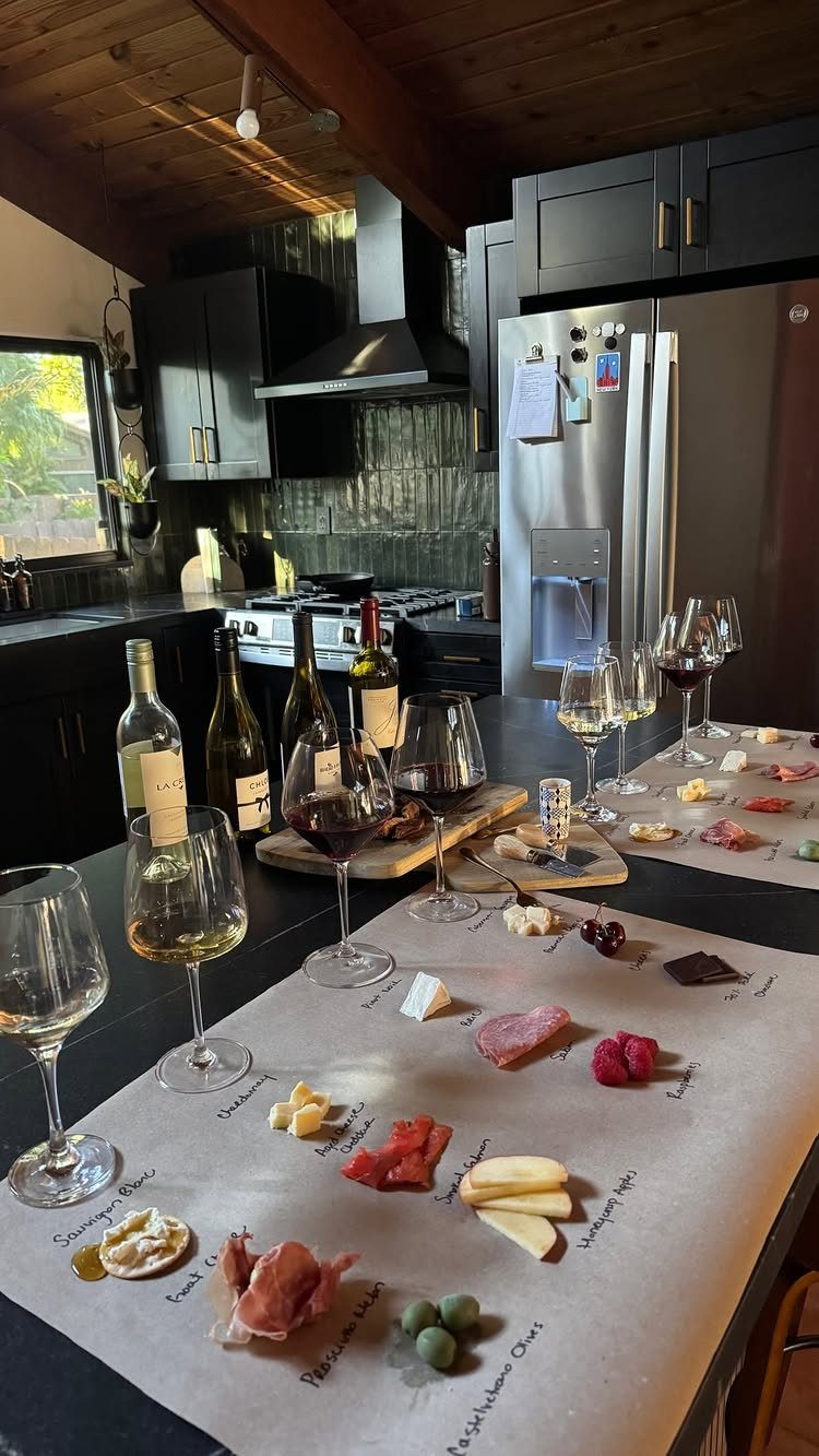 Wine tasting spread with bottles, glasses, and labeled charcuterie on a kitchen counter.