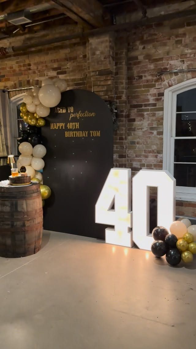 40th birthday party decorations with large glowing numbers, balloons, and a black backdrop.
