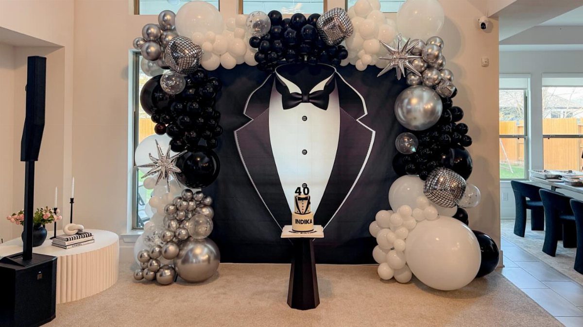 Tuxedo backdrop with black, white, and silver balloon arch and 40th birthday cake.
