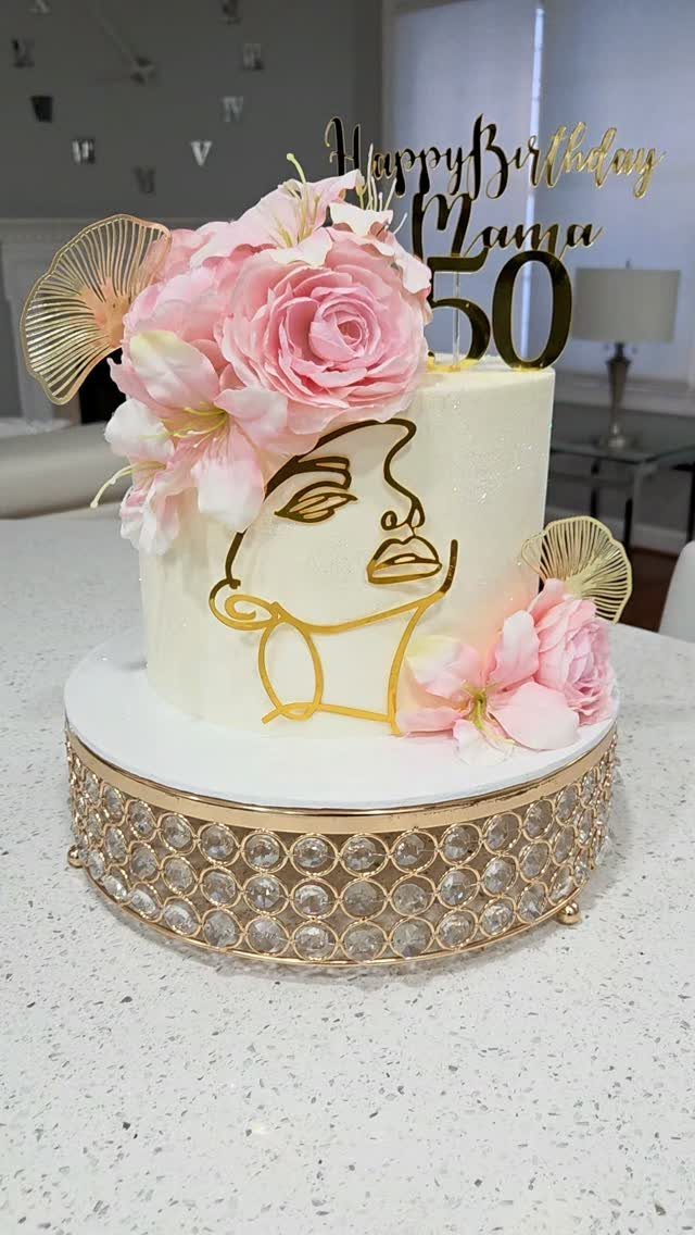 White birthday cake with pink flowers, gold face art, and 50 topper.