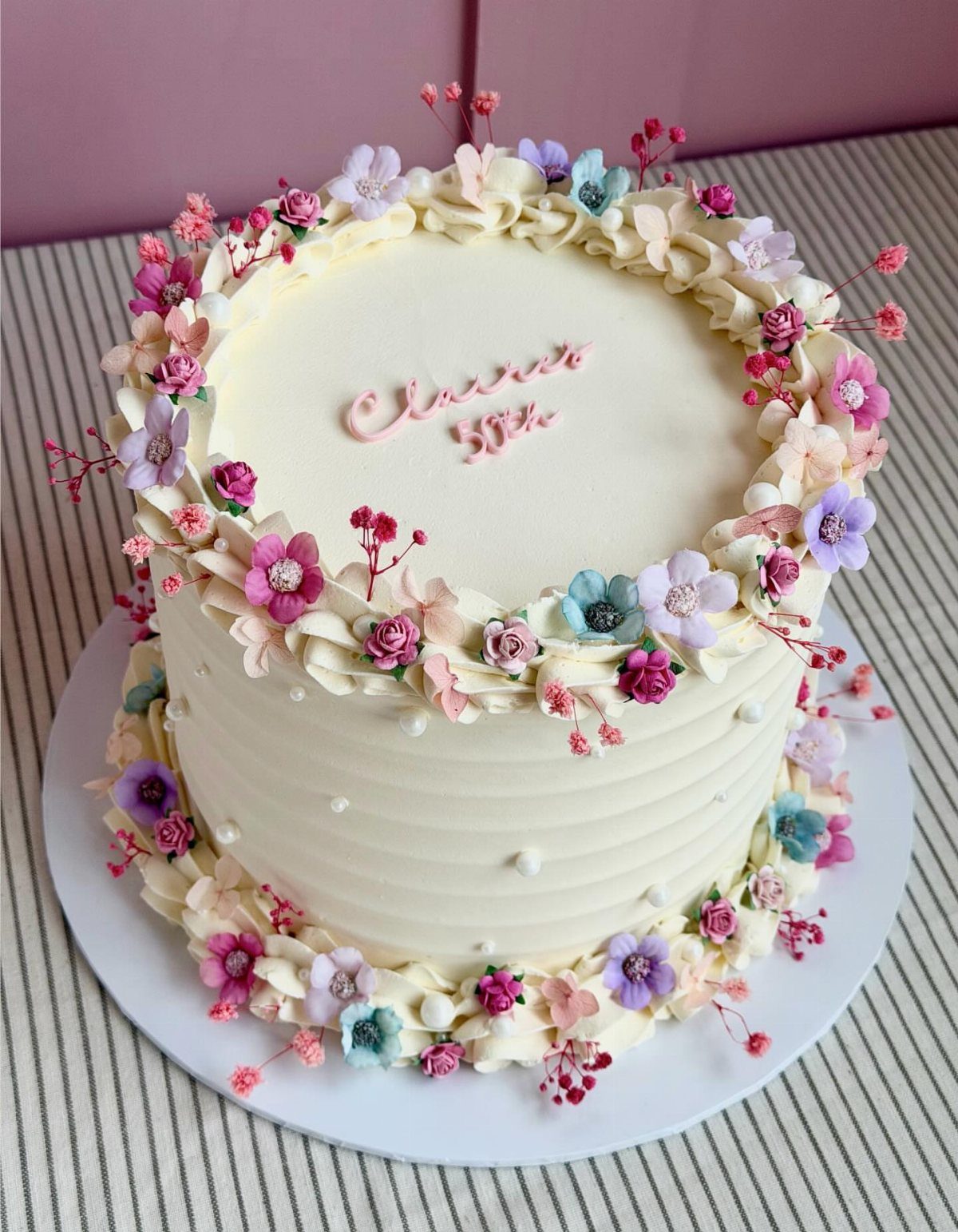 White frosted cake decorated with small colorful flowers and berries on a striped surface