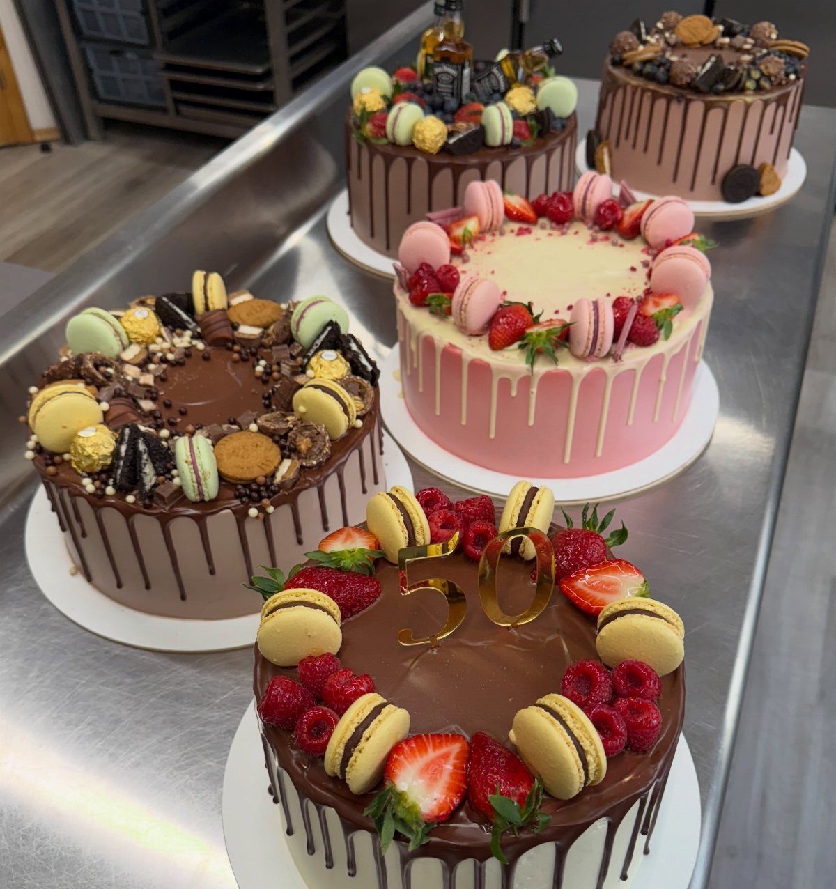 Four decorated drip cakes, including one with a gold 50 topper and strawberries.