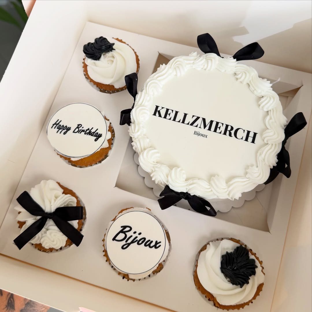White birthday cake with black bows and matching cupcakes in a white box
