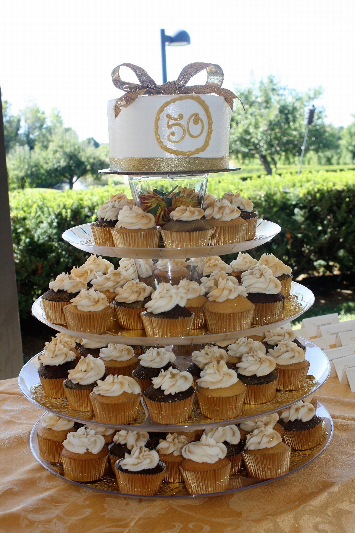 Cupcake tower with a small white cake on top featuring a gold 50.