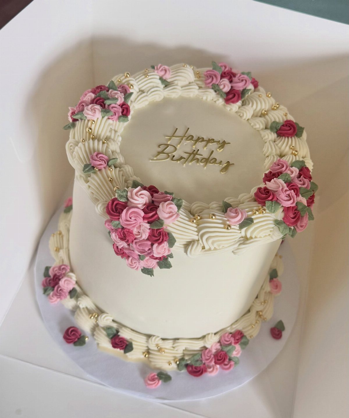 White birthday cake decorated with pink buttercream roses and gold pearl accents.