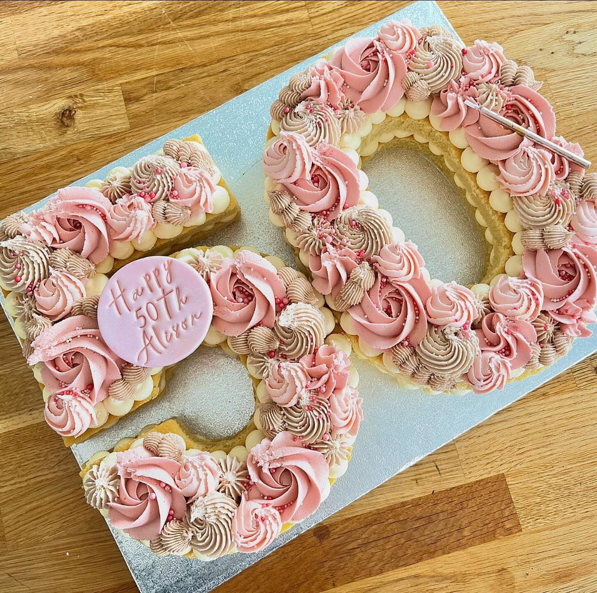 Number 50 cake decorated with pink and taupe buttercream rosettes and silver pearls.
