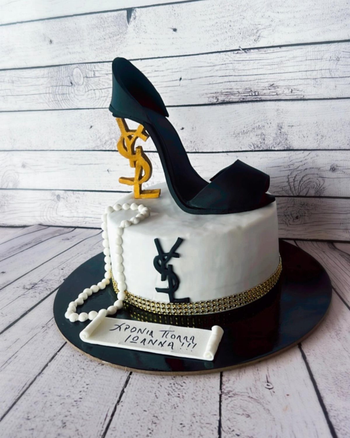 White cake topped with a black fondant high heel and gold YSL logo.