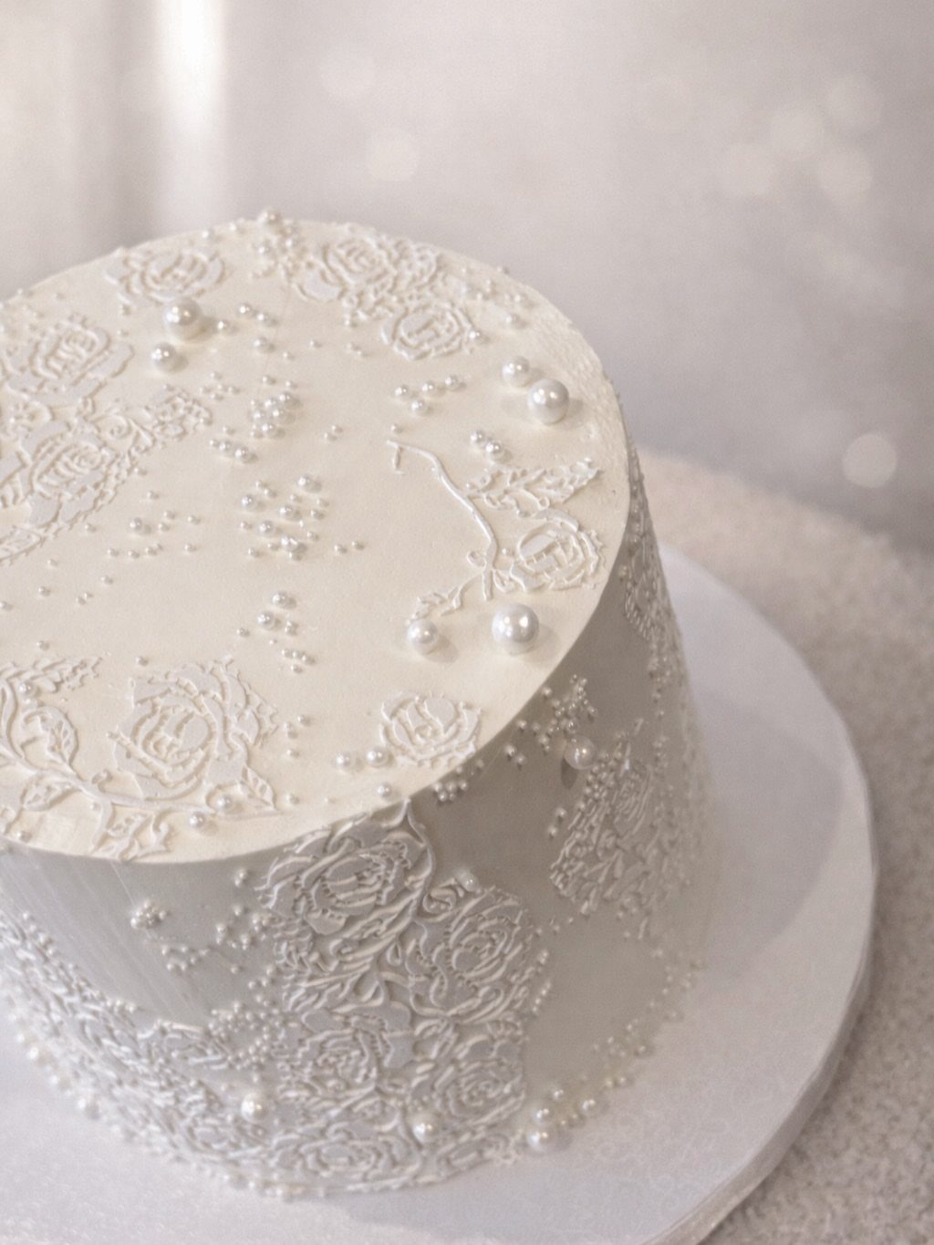 White cake decorated with intricate lace patterns and small white edible pearls.