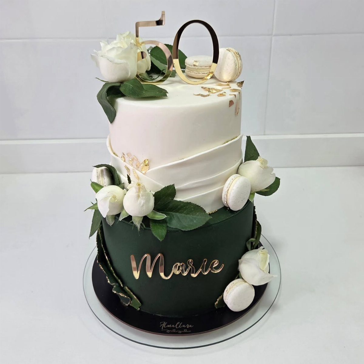 Two-tier green and white cake decorated with white peonies, macarons, and gold 50 topper.