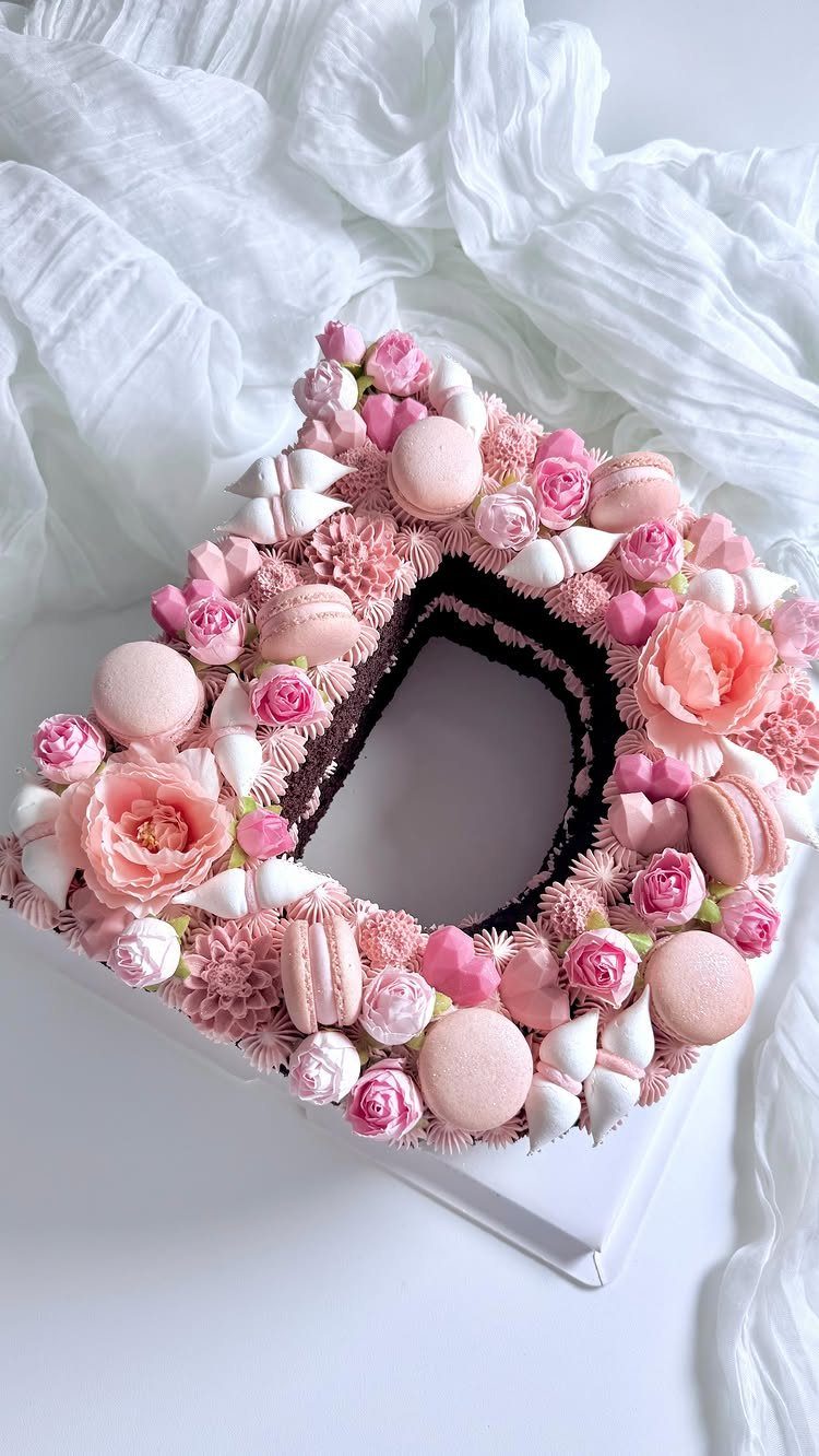 Heart-shaped monogram cake decorated with pink macarons and delicate pink roses.