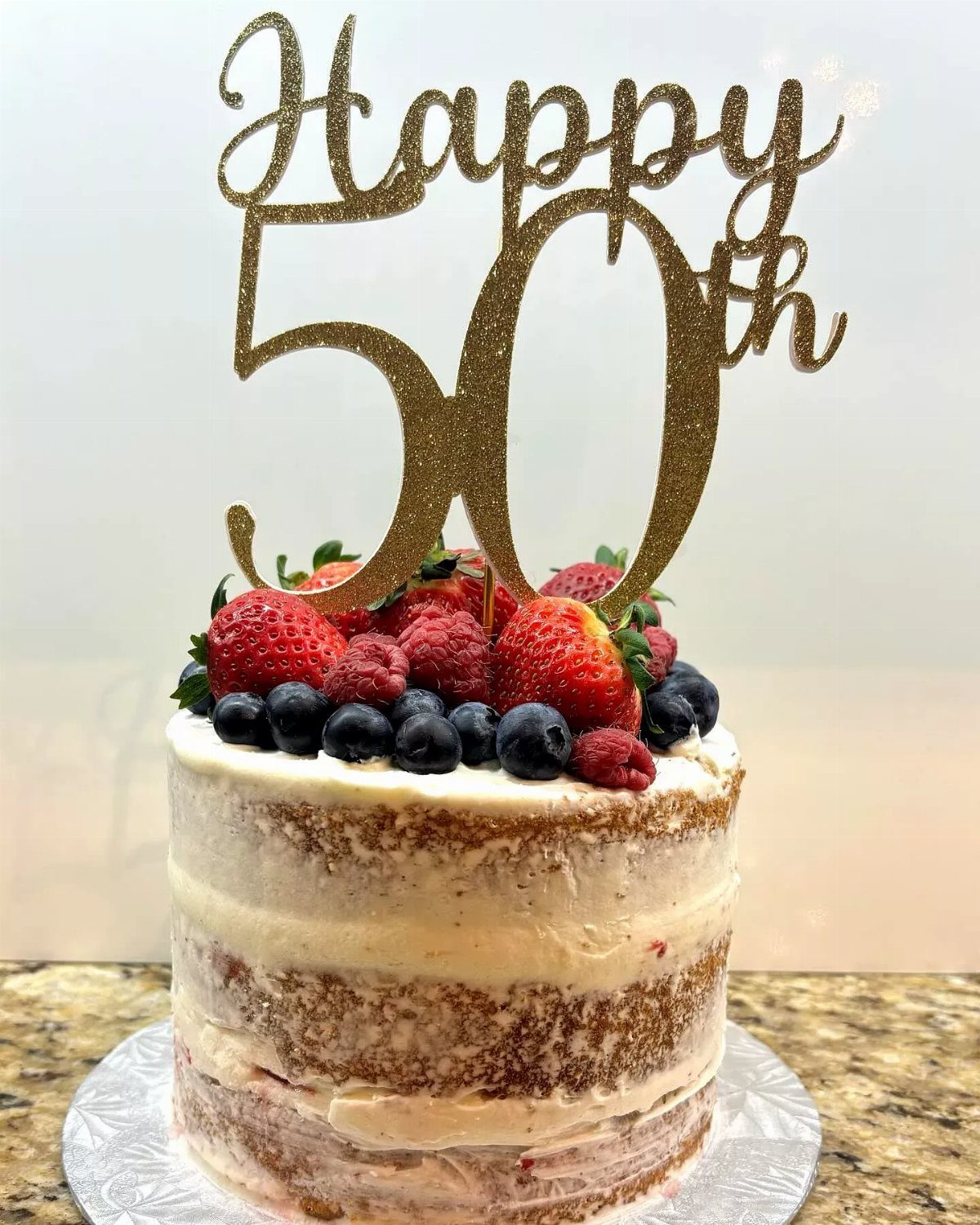 Semi-naked layer cake topped with fresh berries and a gold Happy 50th topper.