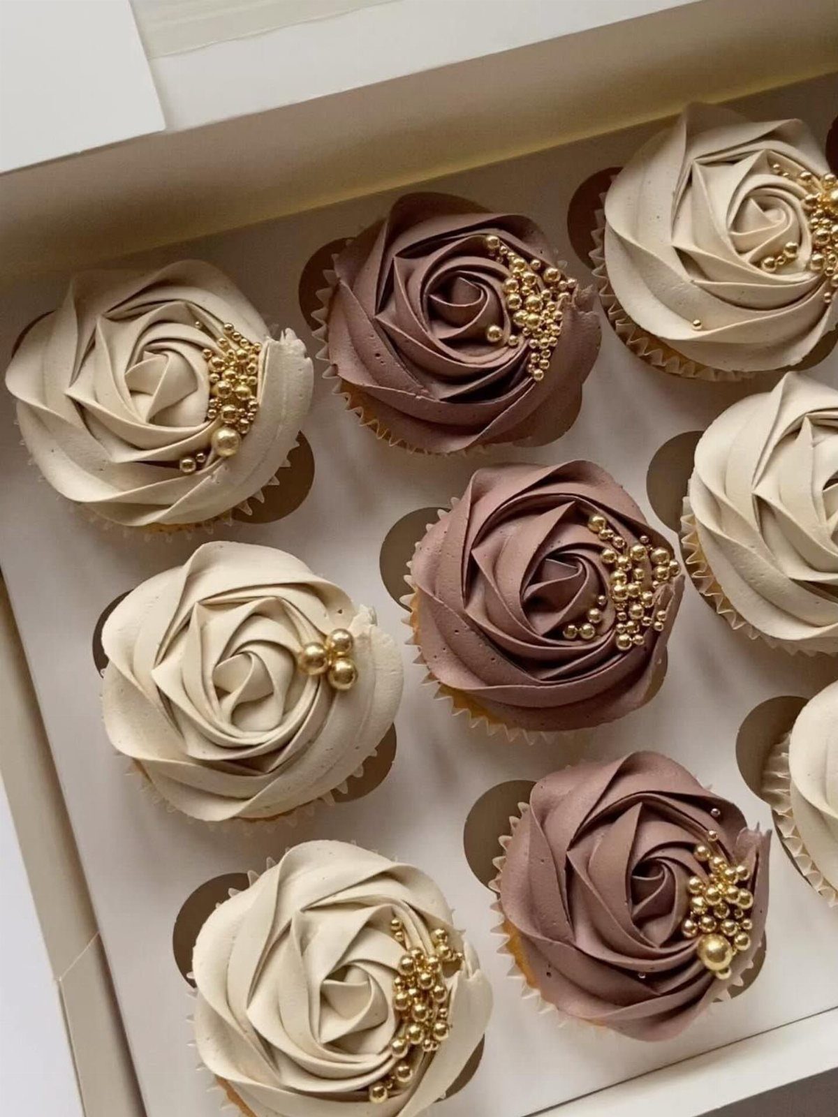 Rose-shaped cupcakes in cream and mauve with gold pearls in a white box