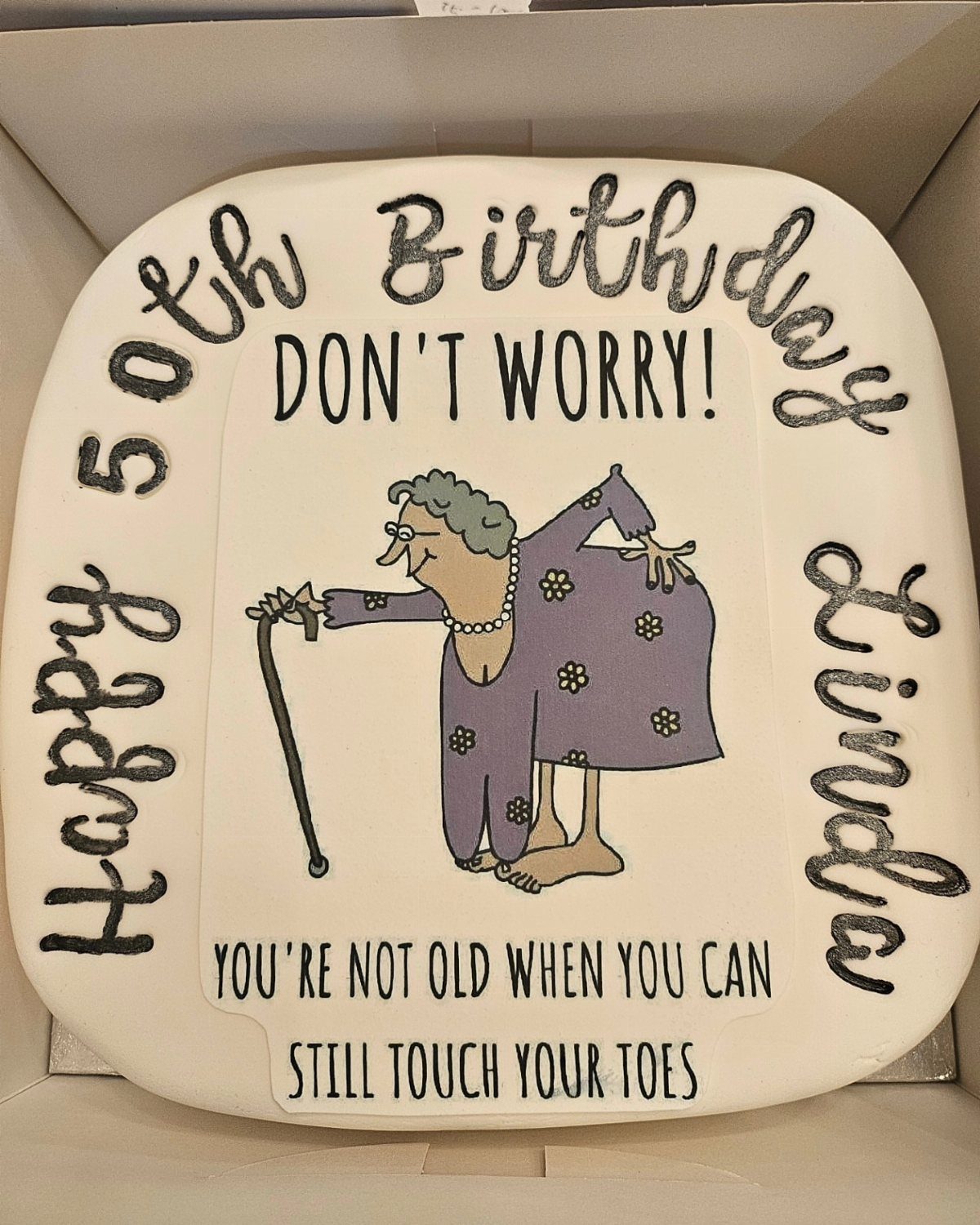 Tombstone-shaped 50th birthday cake with a cartoon elderly woman and humorous text.