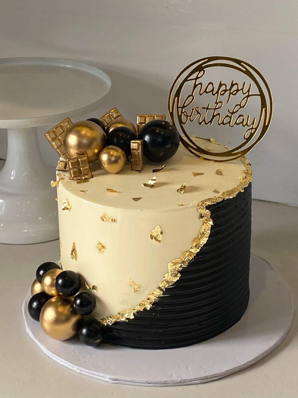 Split cream and black birthday cake decorated with gold leaf and spheres.