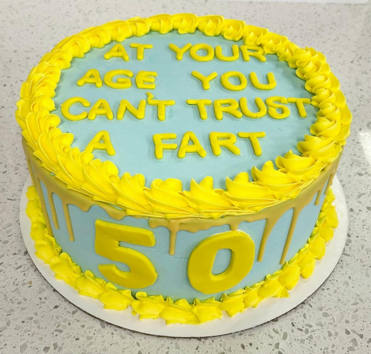 Light blue cake with yellow frosting and text about aging and number 50