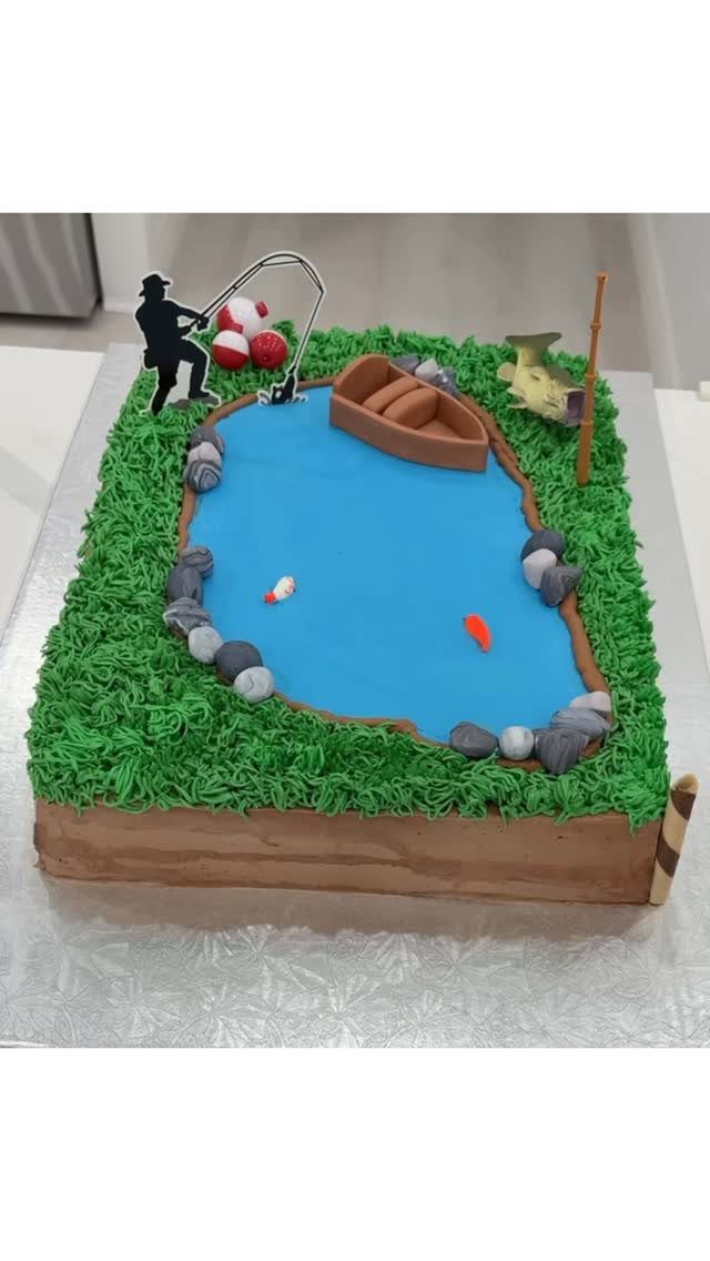 Fishing themed cake with a blue pond, green grass, and a fisherman silhouette.