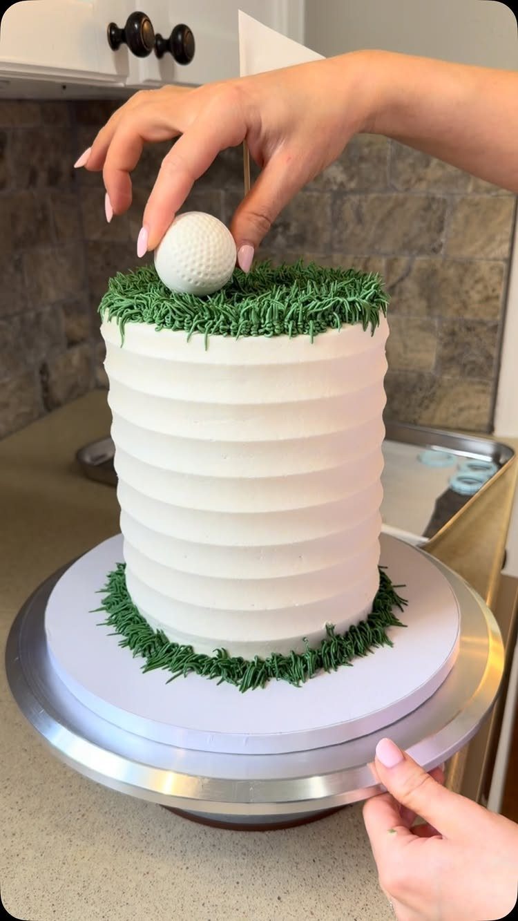 White ridged cake with green frosting grass and a golf ball on top.