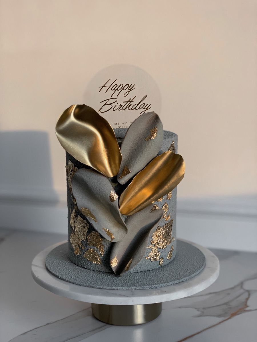 Grey birthday cake with gold and grey chocolate shards and a Happy Birthday topper