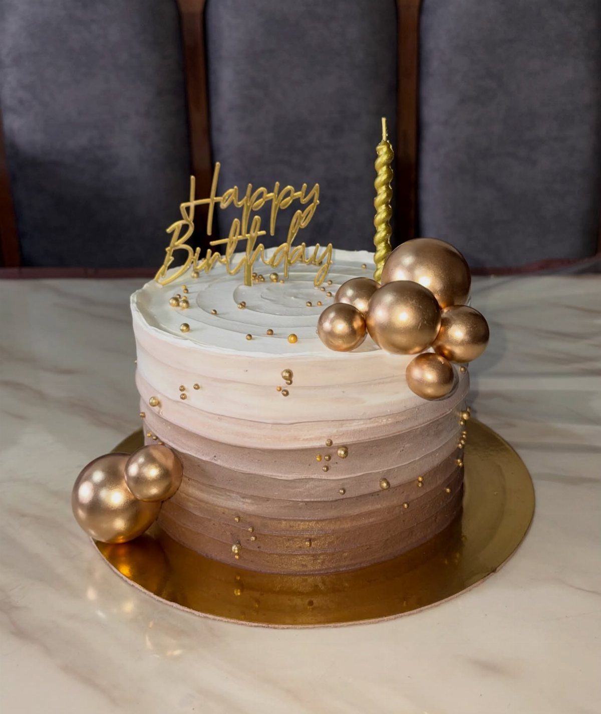 Ombre birthday cake with brown to white gradient frosting and gold decorations.