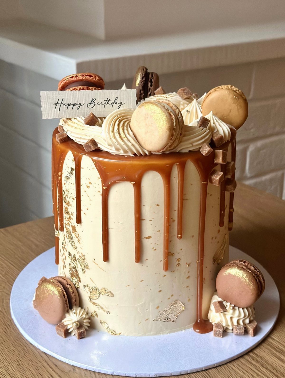 Cream cake with caramel drip, macarons, and frosting swirls on a white base.