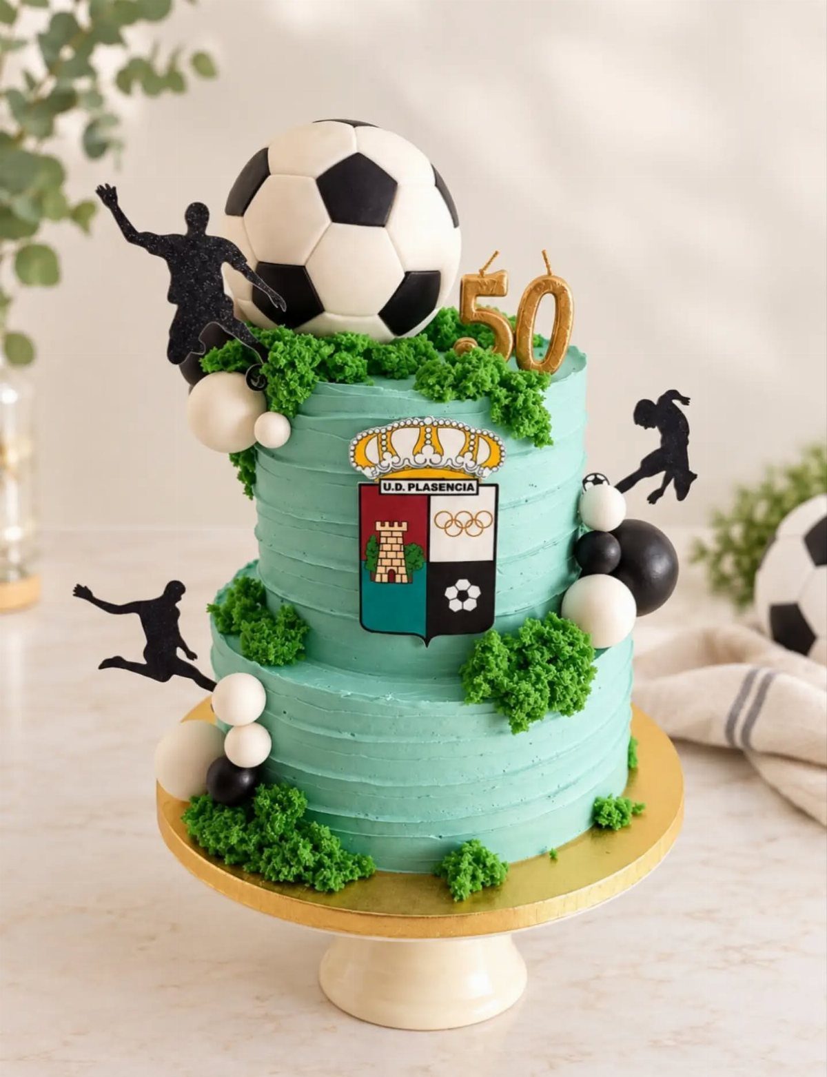 Two-tier blue soccer cake with a soccer ball topper and gold 50 candles.