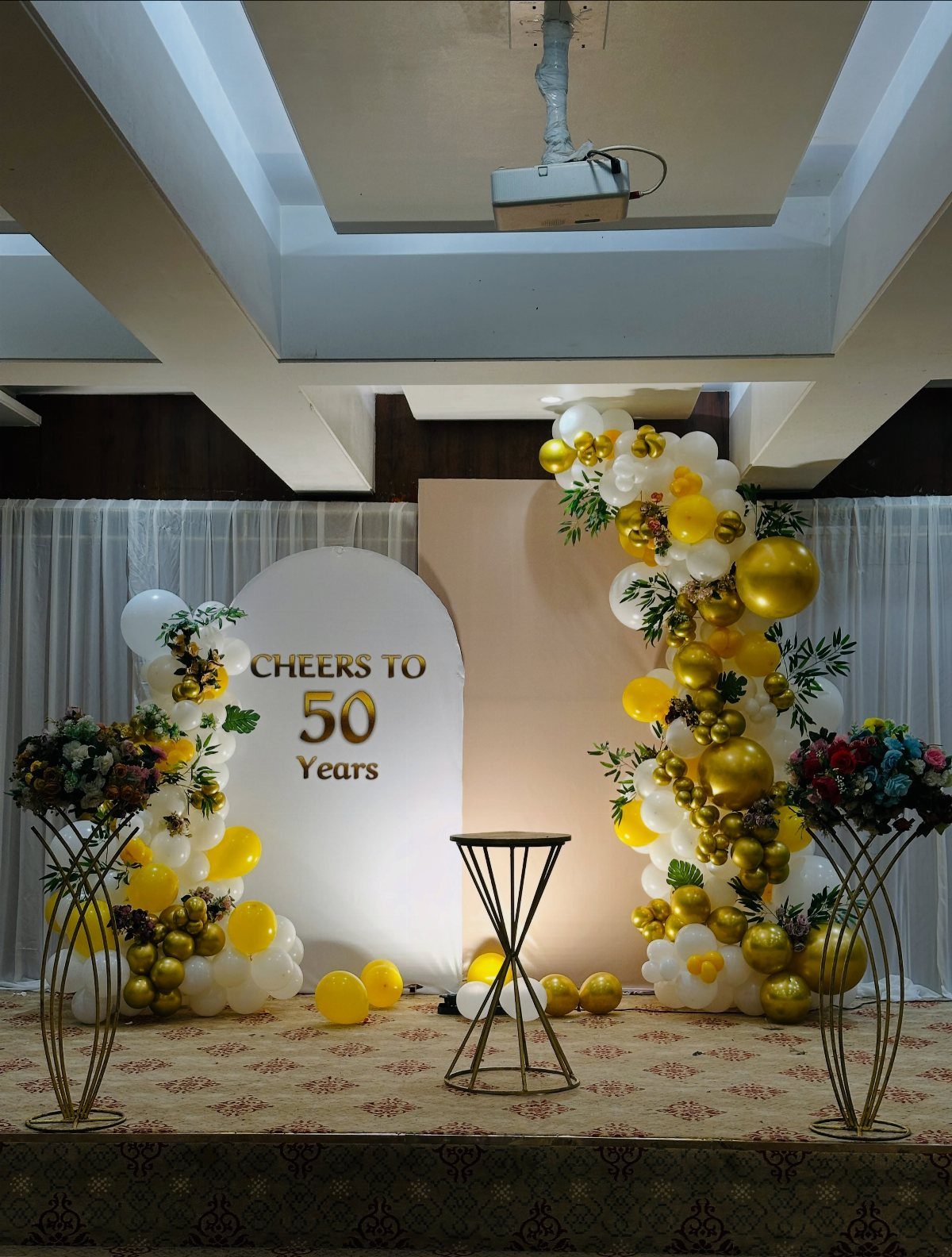 Gold and white balloon arch with Cheers to 50 Years backdrop on stage