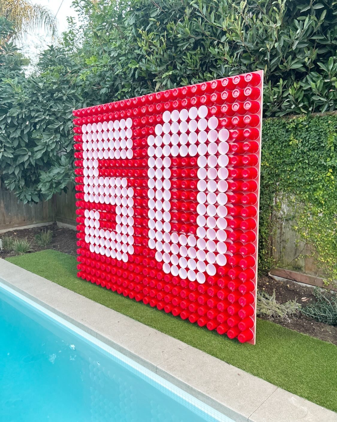 Wall of red and white plastic cups forming the number 50 by a pool