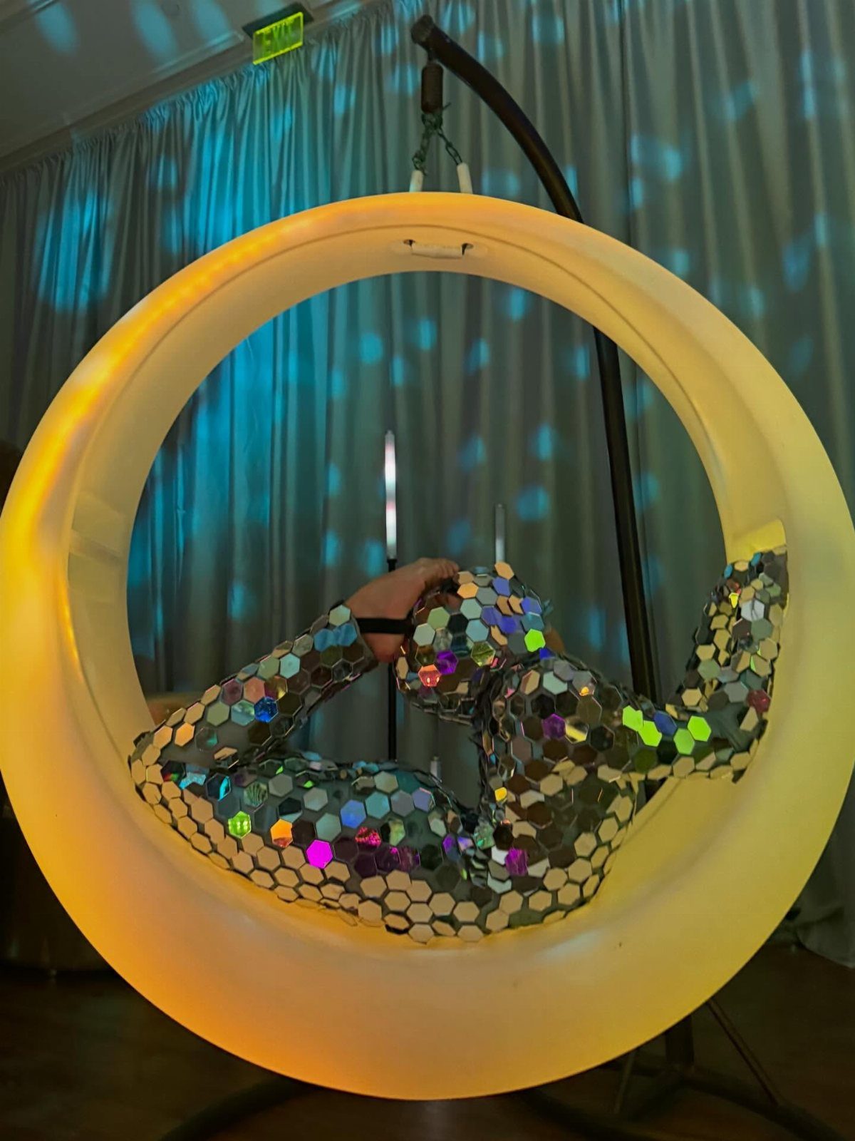 Aerial performer in mirrored bodysuit performing inside a glowing yellow circular hoop