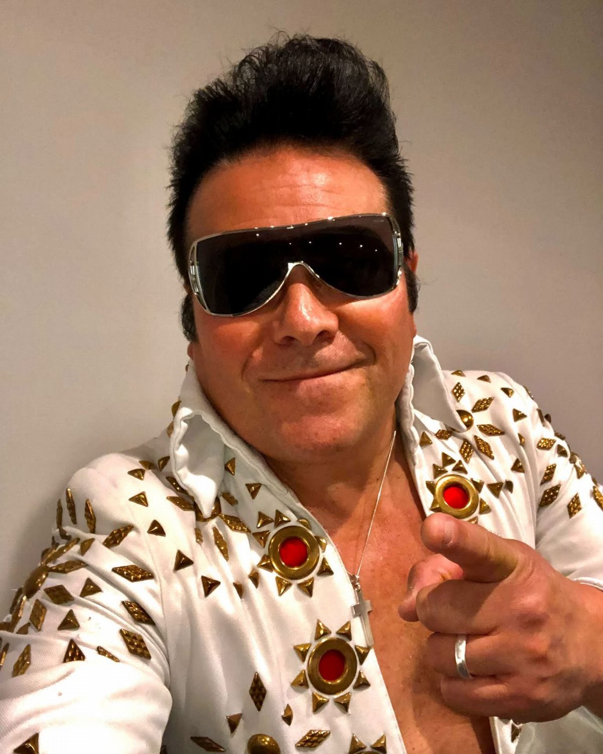 Man dressed as Elvis Presley in a white studded jumpsuit and sunglasses pointing forward.