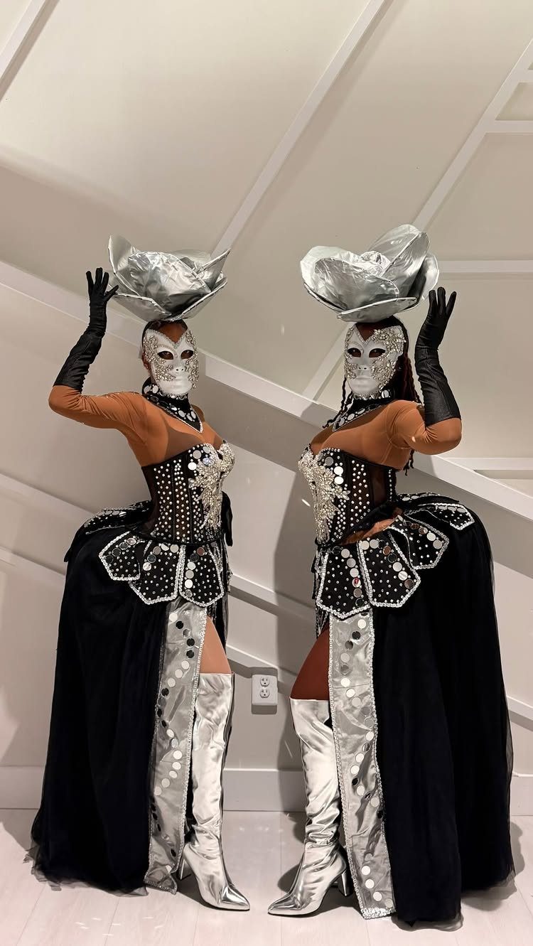 Two performers in silver masks and ornate black and silver costumes posing indoors.