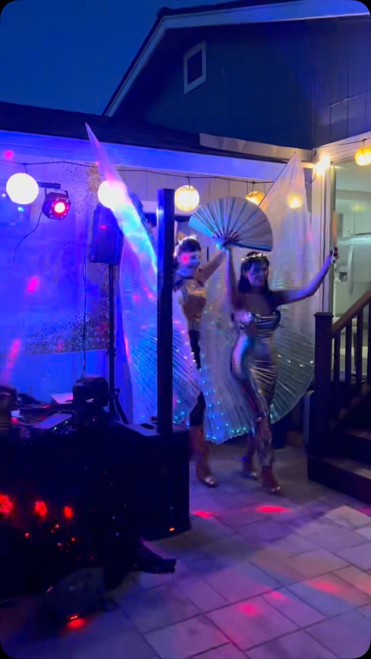 Two performers in gold costumes with large fans at an outdoor party.