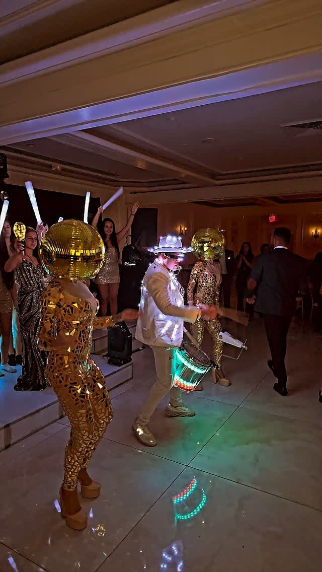 Performers in gold sequined suits and helmets dancing at a formal party event