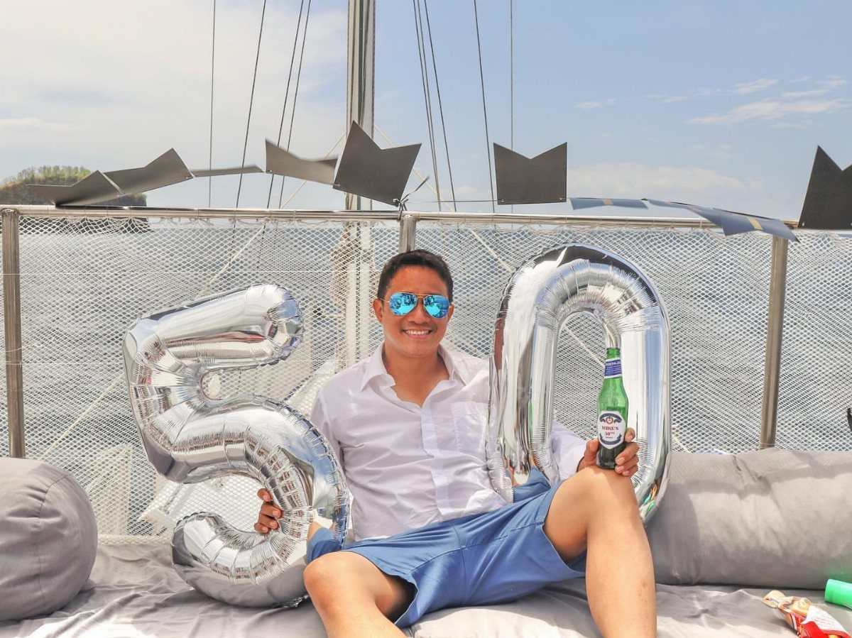 Man celebrating 50th birthday on a yacht with silver number balloons and beer.